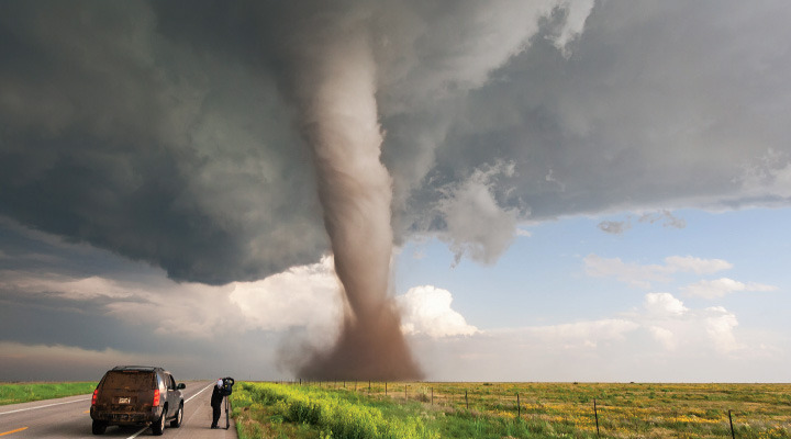Photo of a person next to their car and taking a photo of a large tornado